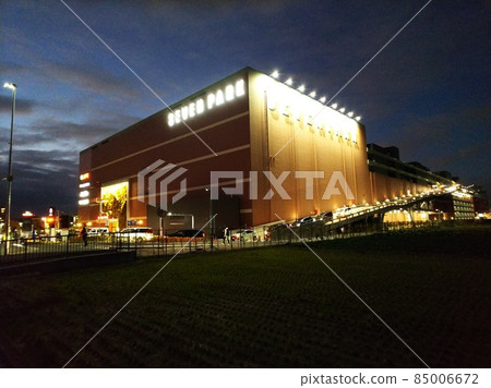 Headlights of cars lined up in a string at the exit of a large suburban store that emerges in the darkness 85006672