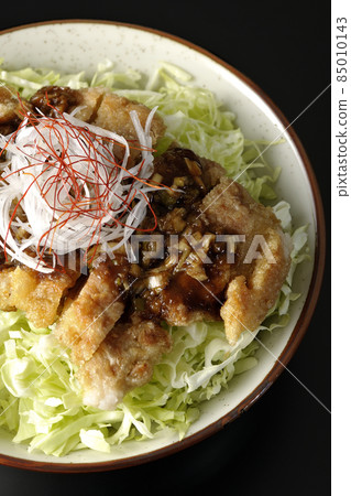 A bird's-eye view of white-haired green onions, red pepper, shredded cabbage, and deep-fried chicken with soy sauce on a black background. 85010143