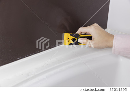 A person who is scraping the scale of the bathroom wall with a scraper 85011295