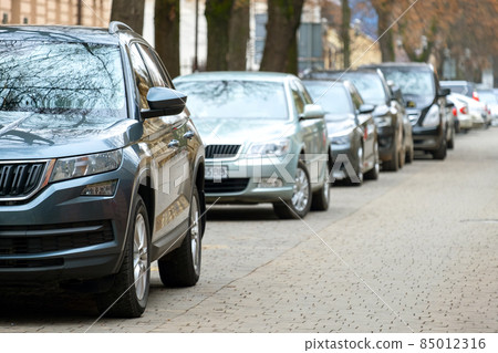 Cars parked in a row on a city street side. 85012316