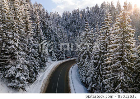 Aerial view of winter landscape with snow covered mountain hills and winding forest road in morning. 85012635