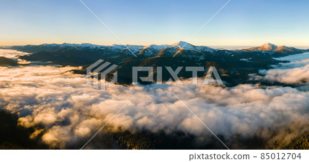 Aerial view of vibrant sunrise over white dense fog with distant dark Carpathian mountains on horizon. 85012704