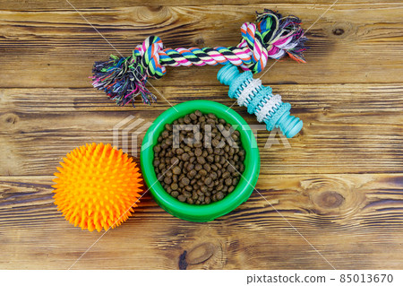 Dog toys and feed for dogs in green plastic bowl on wooden background. Top view. Dog care concept Dog toys and feed for dogs in green plastic bowl on wooden background. Top view. Dog care concept 85013670