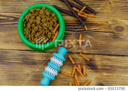Dog toy, delicacy food and feed for dogs in green plastic bowl on wooden background. Top view. Dog care concept 85013700