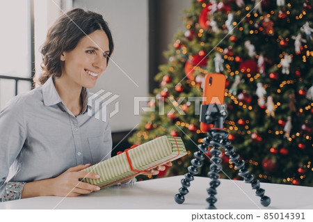 Smiling positive female blogger recording video tutorial about tips for wrapping Christmas presents Smiling positive female blogger recording video tutorial about tips for wrapping Christmas presents 85014391