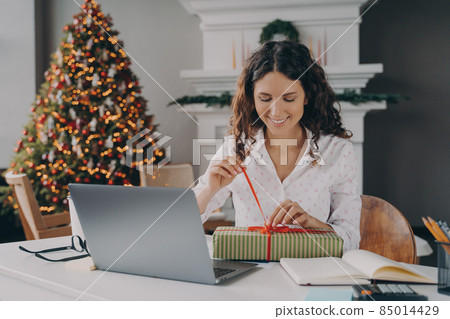 Young happy excited european woman office worker unpacking Christmas present at work 85014429