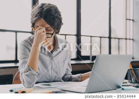 Overworked business lady suffering from headache while working remotely from home 85014444