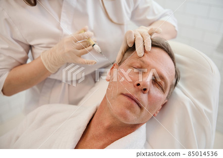 Beautician performs thread lifting according to the lines drawn on the mature handsome man's face. Rejuvenation, anti aging therapy concept for men in a modern spa clinic. Men's injection cosmetology Beautician performs thread lifting according to the lines drawn on the mature handsome man's face. Rejuvenation, anti aging therapy concept for men in a modern spa clinic. Men's injection cosmetology 85014536