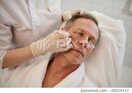 Cosmetologist drawing guidelines for cosmetic product injection. Thread facelift with arrows for male skin, facial contouring procedure with meso threads for facial rejuvenation. Men's cosmetology Cosmetologist drawing guidelines for cosmetic product injection. Thread facelift with arrows for male skin, facial contouring procedure with meso threads for facial rejuvenation. Men's cosmetology 85014537