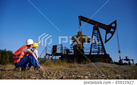 Back view of technician talking with capable boy about mining maintenance during work time at drilling rig, father and son discussing business extraction at earthwork and service for pump construction Back view of technician talking with capable boy about mining maintenance during work time at drilling rig, father and son discussing business extraction at earthwork and service for pump construction 85015927