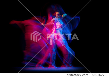 Emotional young girl in white costume dancing hip-hop dance isolated on dark background at dance hall in neon mixed light. Emotional young girl in white costume dancing hip-hop dance isolated on dark background at dance hall in neon mixed light. 85016279