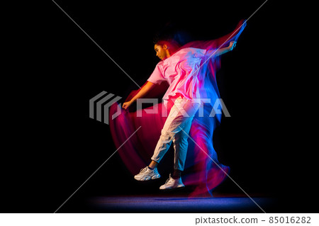 Stylish young girl in white costume dancing hip-hop dance isolated on dark background at dance hall in neon mixed light. Stylish young girl in white costume dancing hip-hop dance isolated on dark background at dance hall in neon mixed light. 85016282