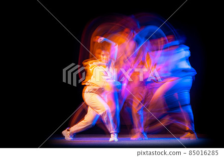 Excited young girl in white costume dancing hip-hop dance isolated on dark background at dance hall in neon mixed light. 85016285
