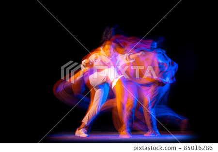 One young sportive girl in white costume dancing hip-hop dance isolated on dark background at dance hall in neon mixed light. 85016286