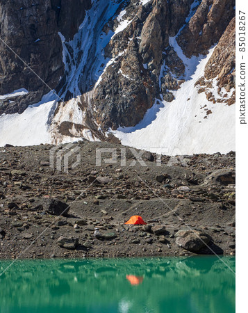 Camping near a glacial mountain lake, distant view. Mountaineering camp at the Blue Lake. Aktru mountain range, Altai. Vertical view. Camping near a glacial mountain lake, distant view. Mountaineering camp at the Blue Lake. Aktru mountain range, Altai. Vertical view. 85018267