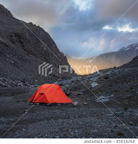 Square view of surrealist alpine landscape with tent on rocky hill among rocks in sunrise. Beautiful morning mountains in low clouds. Surreal scenery with tent in highlands in overcast weather. Square view of surrealist alpine landscape with tent on rocky hill among rocks in sunrise. Beautiful morning mountains in low clouds. Surreal scenery with tent in highlands in overcast weather. 85018268