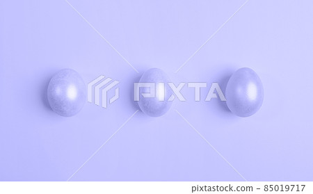 Three glossy Easter eggs are lying in row. Creative minimal festive Easter background. Trendy toning in color of year lavender Very Peri. View from above. Flat lay, copy space. 85019717