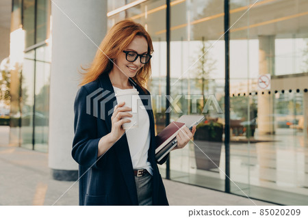 Smiling redhead woman corporate worker dressed in formal clothes drinks coffee 85020209