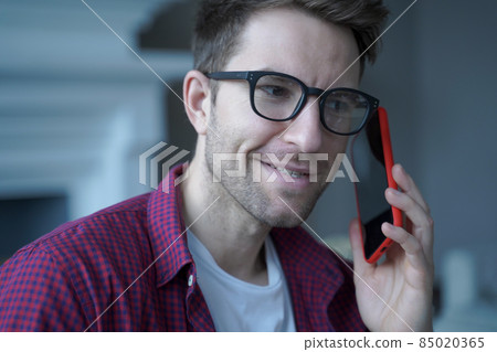 Young smiling german guy in glasses using mobile phone and talking on with friend Young smiling german guy in glasses using mobile phone and talking on with friend 85020365