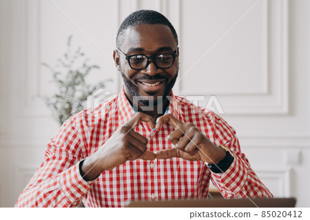 Happy african man gesturing heart symbol shape with hands during video call with family 85020412