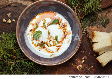 Eating Turkish poached eggs or Cilbir on a bed of light yoghurt topped with chilli oil, pistachios and mint leaves. Eating Turkish poached eggs or Cilbir on a bed of light yoghurt topped with chilli oil, pistachios and mint leaves. 85020554