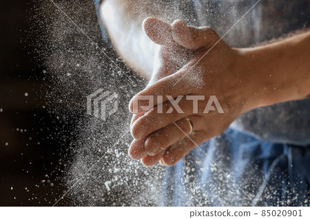 Male baker lightly flouring proofing basket for home made sourdough bread. 85020901