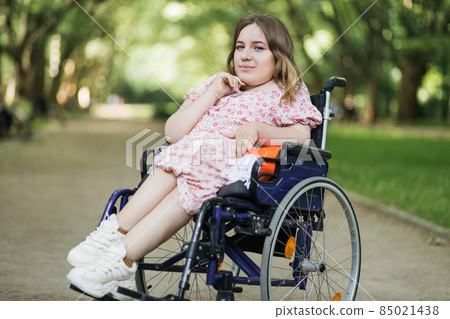 Beautiful woman in wheelchair looking at camera outdoors Beautiful woman in wheelchair looking at camera outdoors 85021438
