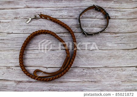 Brown leather leash and spiked collar for dog on wooden background. Top view 85021872