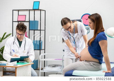Your doctor auscultates a pregnant patient's abdomen with a stethoscope. The attending physician completes the appointment calendar. Your doctor auscultates a pregnant patient's abdomen with a stethoscope. The attending physician completes the appointment calendar. 85022588