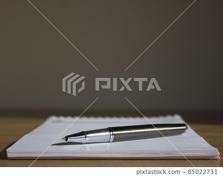 Business and office work symbol. White notebook and pen on beautiful wood table. Warm sunlight. Beautiful grey background. Business and office work concept. 85022731