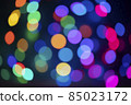 Defocused Christmas lights of blue, red, yellow and green with shades of very peri from a multicolored garland hugging the sphere 85023172