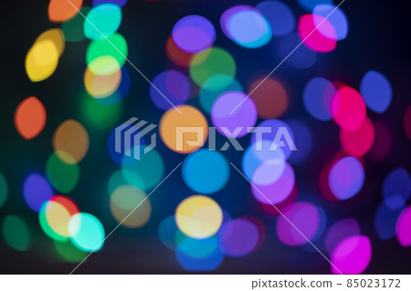 Defocused Christmas lights of blue, red, yellow and green with shades of very peri from a multicolored garland hugging the sphere Defocused Christmas lights of blue, red, yellow and green with shades of very peri from a multicolored garland hugging the sphere 85023172