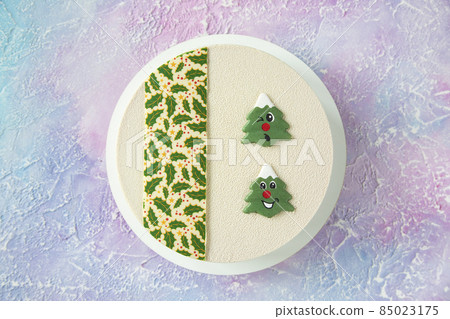 Beautiful and delicious white designer Christmas cake on the table with winter frosty pink and blue patterns with beautiful smiling Christmas trees in the form of chocolate cookies - top view Beautiful and delicious white designer Christmas cake on the table with winter frosty pink and blue patterns with beautiful smiling Christmas trees in the form of chocolate cookies - top view 85023175