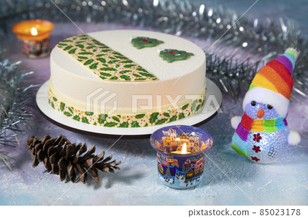 New Year's snowman in a scarf and a rainbow - colored hat with a Christmas Eve chocolate cake with beautiful Christmas tree cookies and Christmas decor - candles, pine cones, tinsel New Year's snowman in a scarf and a rainbow - colored hat with a Christmas Eve chocolate cake with beautiful Christmas tree cookies and Christmas decor - candles, pine cones, tinsel 85023178