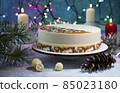 Festive New Year's cake for Christmas or Christmas Eve with beautiful decorations on a winter background with burning candles and a garland with colorful lights 85023180