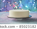 Christmas cake made of white chocolate with velour on the table against the background of festive lights garlands. The table and background are frosty patterns - close-up 85023182