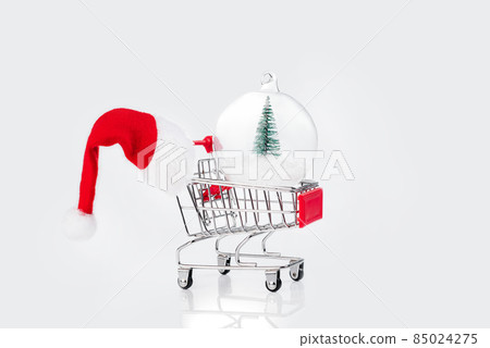 Christmas sale.Soft focus.Snow Ball.Supermarket trolley with new year glass ball and santa hat on a light background.Christmas,New Year background.Christmas glass ball with a miniature Christmas tree. Christmas sale.Soft focus.Snow Ball.Supermarket trolley with new year glass ball and santa hat on a light background.Christmas,New Year background.Christmas glass ball with a miniature Christmas tree. 85024275