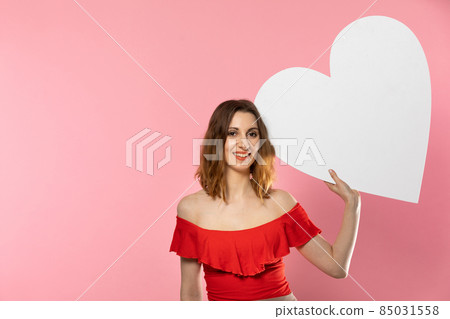 Girl with a large white heart shape in the hands. A student in love stands and holds a large heart shape in her hands. Valentine's Day and love. Girl with a large white heart shape in the hands. A student in love stands and holds a large heart shape in her hands. Valentine's Day and love. 85031558