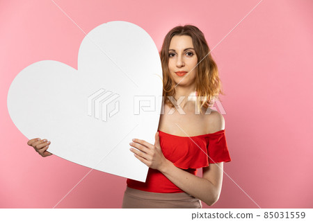 Girl with a large white heart shape in the hands. A student in love stands and holds a large heart shape in her hands. Valentine's Day and love. Girl with a large white heart shape in the hands. A student in love stands and holds a large heart shape in her hands. Valentine's Day and love. 85031559