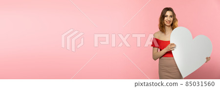 Girl with a large white heart shape in the hands. A student in love stands and holds a large heart shape in her hands. Valentine's Day and love. Panoramic frame. Girl with a large white heart shape in the hands. A student in love stands and holds a large heart shape in her hands. Valentine's Day and love. Panoramic frame. 85031560