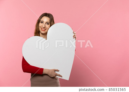Girl with a large white heart shape in the hands. A student in love stands and holds a large heart shape in her hands. Valentine's Day and love. Girl with a large white heart shape in the hands. A student in love stands and holds a large heart shape in her hands. Valentine's Day and love. 85031565