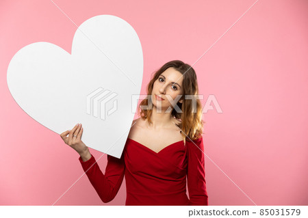 Girl with a large white heart shape in the hands. A student in love stands and holds a large heart shape in her hands. Valentine's Day and love. Girl with a large white heart shape in the hands. A student in love stands and holds a large heart shape in her hands. Valentine's Day and love. 85031579