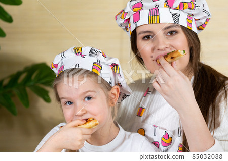Close-up frame. The five-year-old daughter sat down on her mother's lap and together they eat pizza made and baked by themselves. After working together in the kitchen, it's time to eat together. 85032088