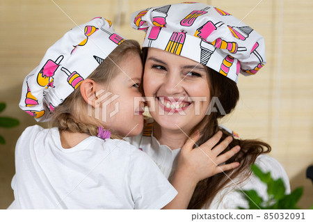 While eating home-made pizza, a five-year-old daughter hugs her mother warmly, thus reciprocating her mother's love for her child. 85032091