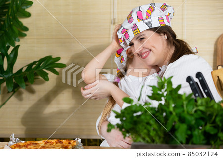 While eating home-made pizza, a five-year-old daughter hugs her mother warmly, thus reciprocating her mother's love for her child. While eating home-made pizza, a five-year-old daughter hugs her mother warmly, thus reciprocating her mother's love for her child. 85032124