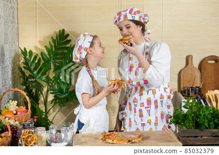 A mother with her five-year-old daughter are eating a pizza prepared and baked by them. Family home-made pizza tasting. After working together in the kitchen, it's time to eat together. A mother with her five-year-old daughter are eating a pizza prepared and baked by them. Family home-made pizza tasting. After working together in the kitchen, it's time to eat together. 85032379
