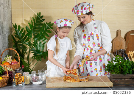An attractive mother with a five-year-old daughter separates the pieces of pizza, which they baked themselves and they want to try it. Puki is hot and fragrant. After working together in the kitchen 85032386