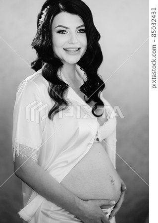 beautiful pregnant bride brunette in white pajamas with bare tummy. beautiful pregnant bride brunette in white pajamas with bare tummy. 85032431