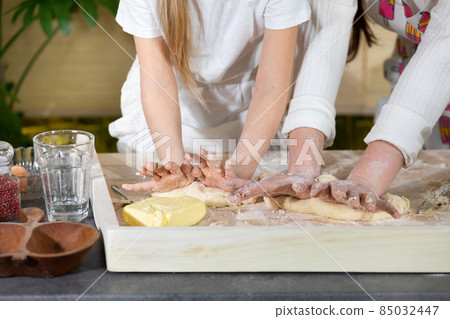 Close-up frame. In one of the last stages, mother and daughter knead and knead a cake that will serve as a pizza cake. Mother and baby do the dough together in the kitchen. Close-up frame. In one of the last stages, mother and daughter knead and knead a cake that will serve as a pizza cake. Mother and baby do the dough together in the kitchen. 85032447