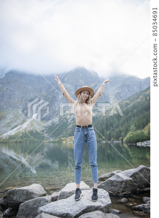 Young tourist woman in a hat with hands up on the top of the mountains 85034691